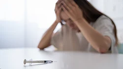 Женщина держится за голову, на столе лежит шприц